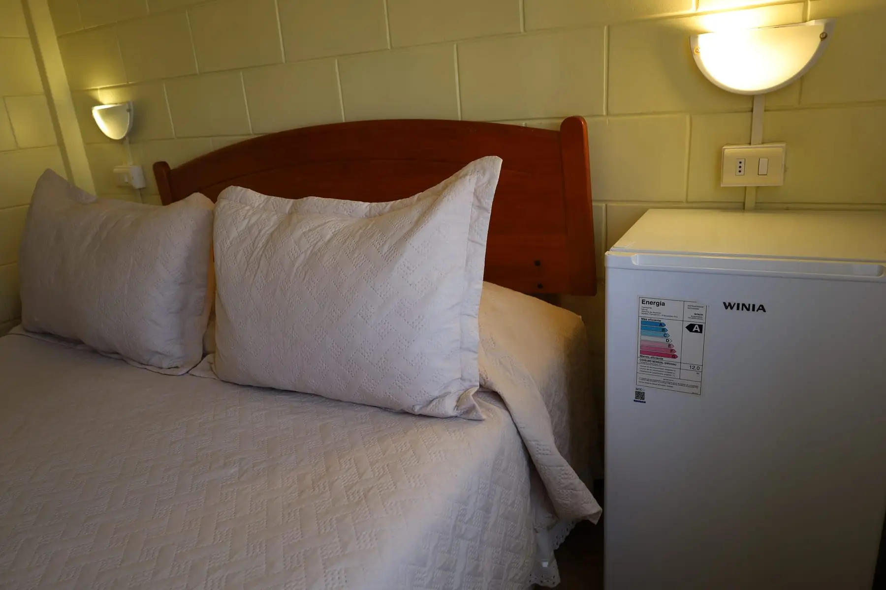 Cama con almohadas y frigobar al costado
